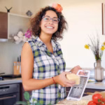 positive-brunette-female-with-curly-hair-makes-salad-with-tomatoes-potato-home-kitchen_613910-13771